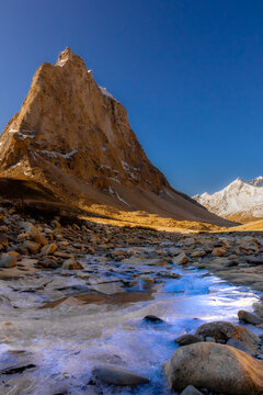 Gonbo Rangjon sacred mountain peak and frozen stream view in Zanskar Ladakh with golden sunlight on rock monolith under blue sky