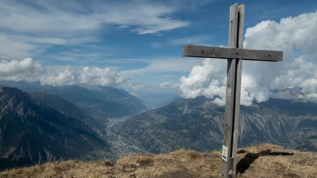 A majestic, weathered wooden summit cross stands prominently on a grassy mountain peak  Folluhorn in the Swiss Alps