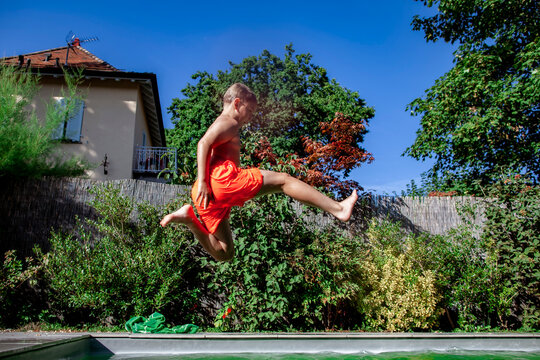 Active boy jumps into a backyard swimming pool on a sunny summer day. Dynamic family lifestyle photo capturing fun, freedom, outdoor recreation and childhood memories.