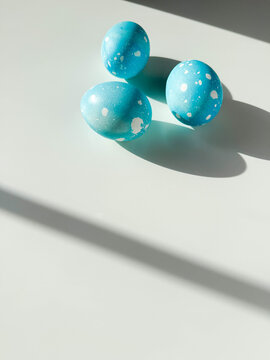 Three Easter eggs colored in sky blue with dots lying on white table with copy space. Festive homemade Easter eggs under bright morning sunlight. Easter traditions, creative decoration