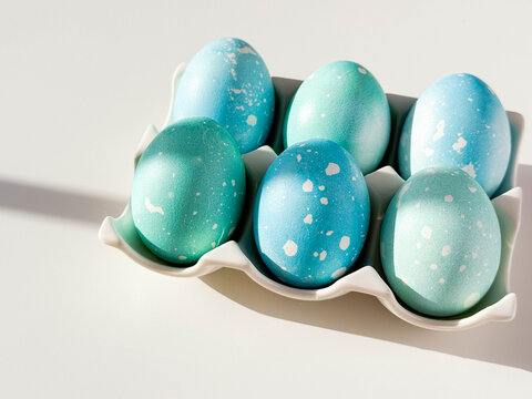 Blue colored Easter eggs with dots on ceramic stand on white table with copy space close up. Festive homemade Easter eggs under bright morning sunlight. Easter traditions, creative decoration