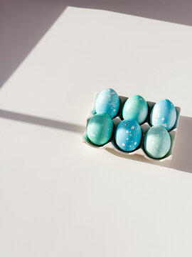 Blue colored Easter eggs with dots on ceramic stand on white table with copy space. Festive homemade Easter eggs under bright morning sunlight. Easter traditions, creative decoration