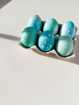 Blue colored Easter eggs with dots on ceramic stand on white table with copy space close up. Festive homemade Easter eggs under bright morning sunlight. Easter traditions, creative decoration
