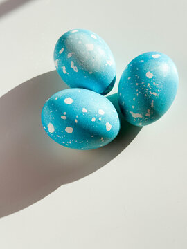 Three Easter eggs colored in sky blue with dots lying on white table with copy space. Festive homemade Easter eggs under bright morning sunlight. Easter traditions, creative decoration