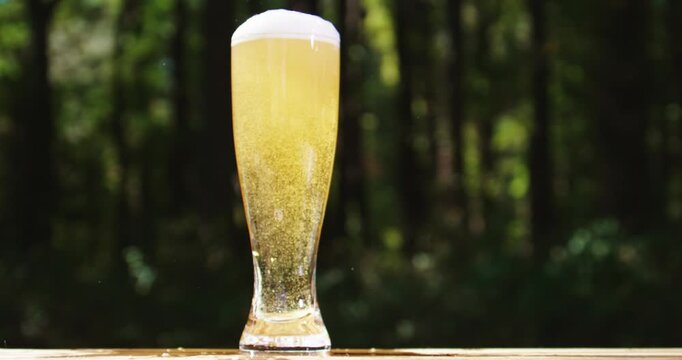 Golden craft beer poured outdoors. Beer splash against green nature background. Pouring amber ale in nature. Brewed beer with bubbles and foam. Craft brewery lager beer on summer day.