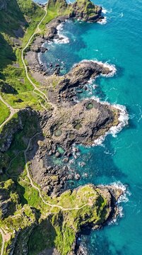 True vertical satellite-style aerial view of Giant's Causeway in spring, highlighting interlocking basalt columns, emerald grasslands, turquoise tidal pools and the Atlantic coastline.