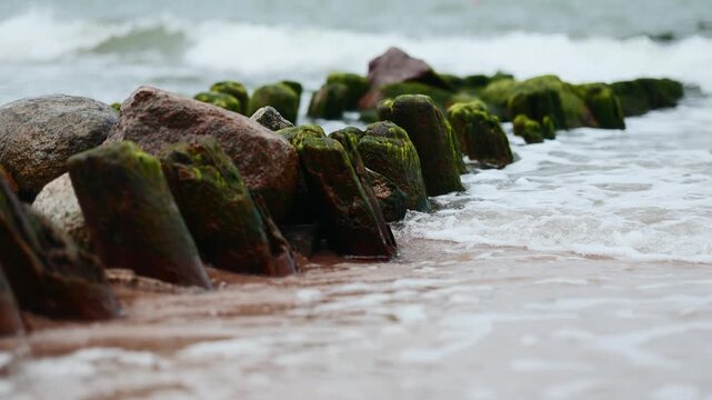 Wooden groyne and protective rocks on sandy beach. Seascape with breakwater extending into stormy sea. Erosion control structure on coastline. Natural scenery for travel concept.