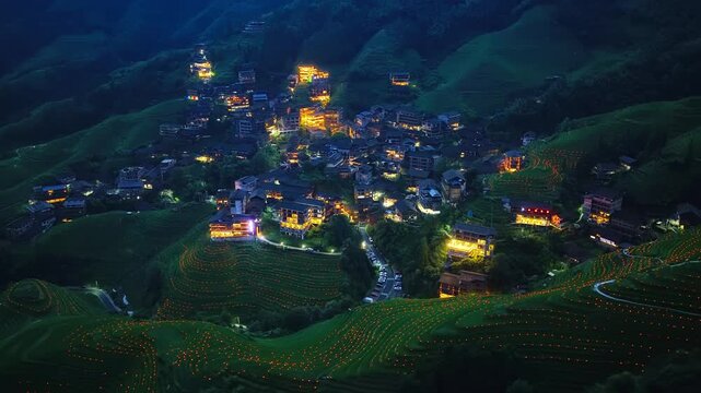 Illuminated village and Longji rice terraces at dusk in Guilin, Guangxi, China.