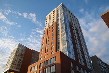 Fototapeta premium New Building facade with brown cladding. Modern apartment building in new development area. Bottom view. Blue sky. Paneling on modern architectural design urban setting. New modern building exterior