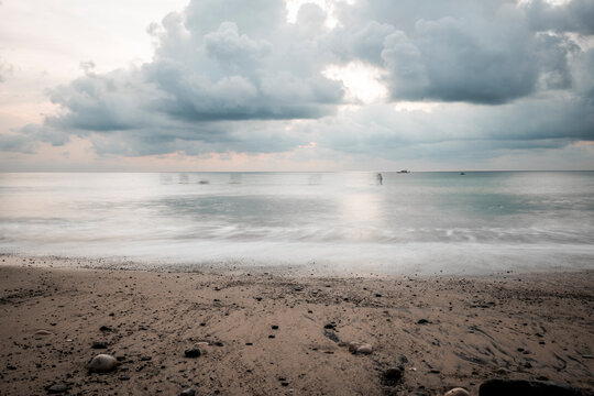 Empty sandy beach and calm sea under dramatic overcast sky with soft light reflecting on wet sand at dawn