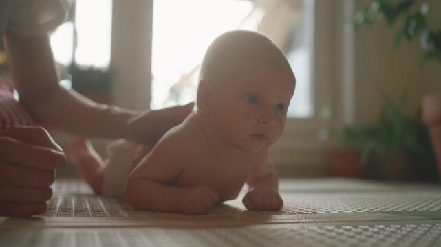 Cute newborn baby with blue eyes learning to hold his head while lying on his stomach during tummy time, with his mother's hands providing gentle support and massage