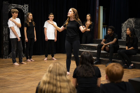 Teen student performs an expressive monologue before classmates during drama class on a school stage, demonstrating confidence, storytelling, and theatrical communication.