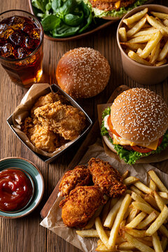 fast food variety on wooden table, assorted fast food meal with burgers fries and snacks, delicious fast food selection served on rustic wooden table