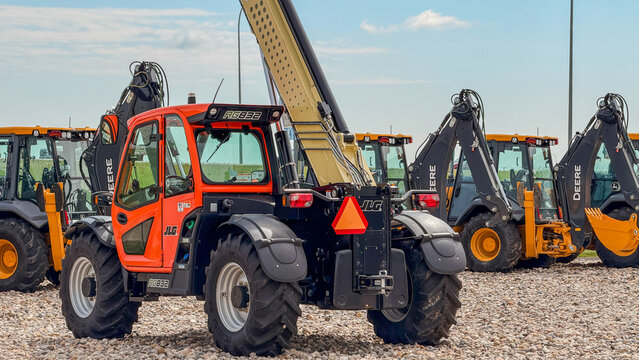 Regina, Canada - July 20, 2026: JLG AG932 telehandler in red and black parked on gravel lot with John Deere backhoe loaders in background