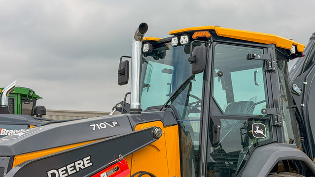 Regina, Canada - July 20, 2026: Close-up of John Deere 710P backhoe loader cab with yellow roof, glass door, exhaust stack and leaping deer logo