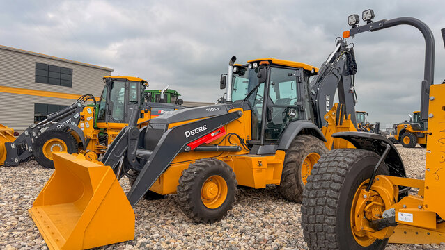 Regina, Canada - July 20, 2026: John Deere 710P backhoe loader parked at equipment dealership lot with multiple yellow construction machines under cloudy sky