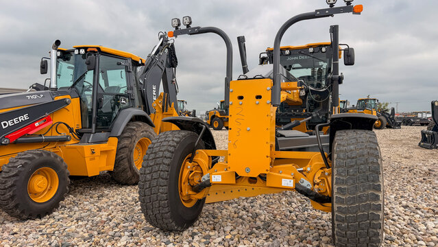 Regina, Canada - July 20, 2026: John Deere 710L backhoe loader and motor grader heavy construction equipment parked on gravel lot under overcast sky