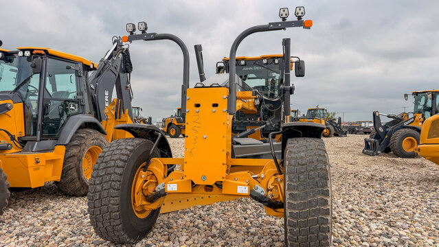 Regina, Canada - July 20, 2026: John Deere motor grader rear axle and tandem wheels displayed at outdoor heavy equipment dealer lot with multiple machines