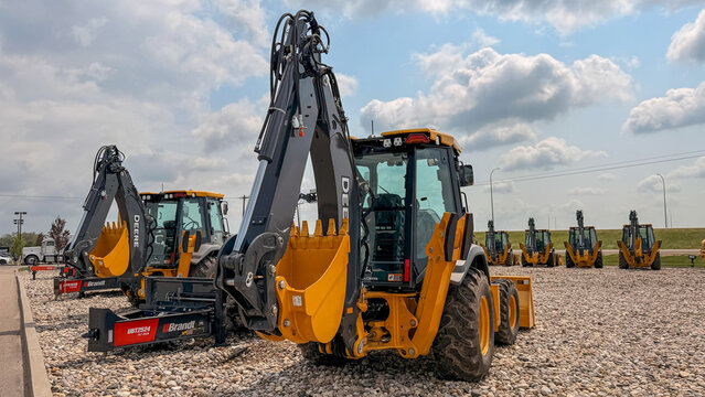 Regina, Canada - July 20, 2026: John Deere backhoe loaders on Brandt equipment dealer lot with hydraulic arms raised against cloudy sky