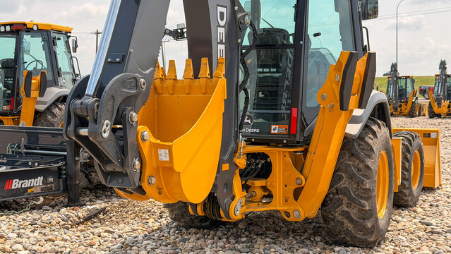Regina, Canada - July 20, 2026: John Deere backhoe loader with yellow bucket and hydraulic arm on gravel lot at Brandt equipment dealership