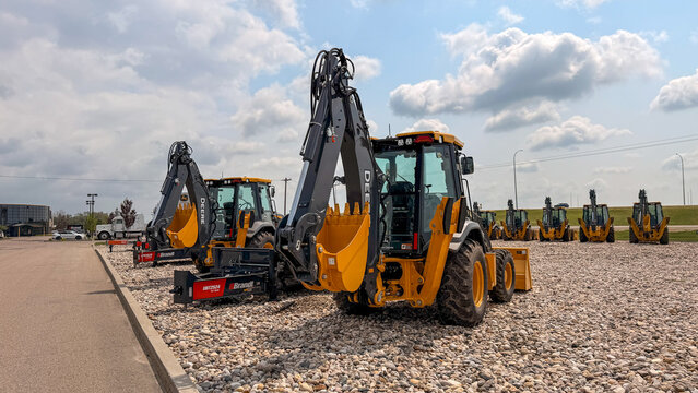 Regina, Canada - July 20, 2026: Row of yellow John Deere backhoe loaders parked on gravel lot at Brandt dealership under partly cloudy sky
