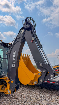 Regina, Canada - July 20, 2026: John Deere backhoe loader arm and yellow excavator bucket raised against blue sky outdoors
