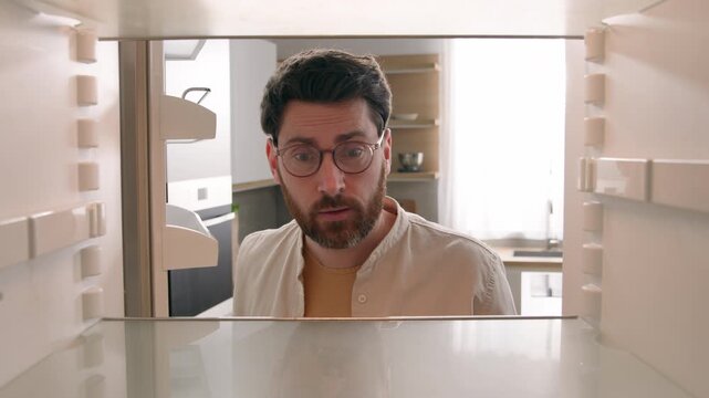 Point of view inside refrigerator hungry Caucasian man looking at empty fridge in kitchen sad disappointed male bachelor homeowner no food without products unemployment crisis food delivery shopping