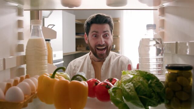 Excited shocked Caucasian man opening full fridge with fresh food cheering in kitchen happy male homeowner guy celebrating healthy vegetables groceries meal delivery lifestyle POV inside refrigerator