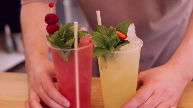 Cold beverages. Fresh drinks. Unrecognizable barman hand using straw mint leaves raspberries with crushed ice at professional bar counter.