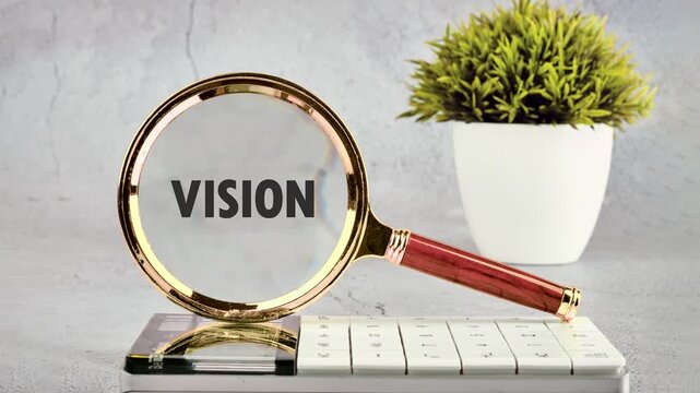 Golden magnifying glass highlights the word Vision on a document while resting on a desk calculator surrounded by a small plant in an indoor office environment
