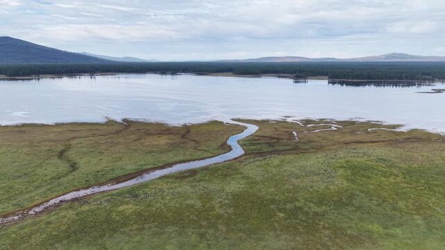Aerial drone orbit over McCoy Flat Reservoir inlet stream, Lassen County, California &mdash; wide view showing reservoir and surrounding meadow on a cloudy day.