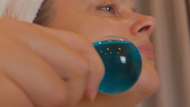 Woman receiving a facial massage with blue cryosphere ice globes, cooling and soothing her skin, enhancing circulation, and promoting relaxation and a healthy glow