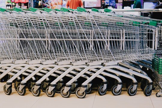 Rows of nested shopping carts stand ready for customers inside a busy supermarket retail entrance area
