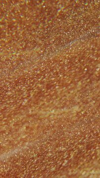 Vertical video. Shimmering flow defocused. Golden fluid. Sparkling paint liquid prism texture. Yellow orange particles spill on color abstract background.