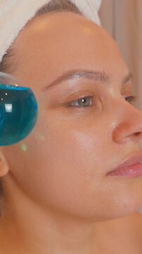 Woman receiving a stimulating cryotherapy facial massage with blue ice globes, revitalizing her skin and promoting a healthy, youthful glow as part of a beauty and self care regimen