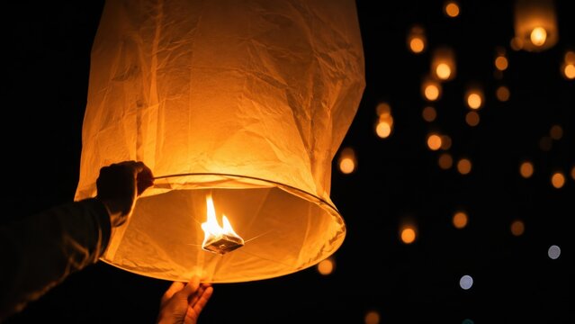 Person holding glowing paper sky lantern for release at night