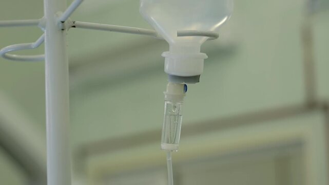 Close-up view of intravenous drip chamber with clear fluid droplets, connected tubing, and metal pole in clinical bedside setting during steady medical infusion treatment