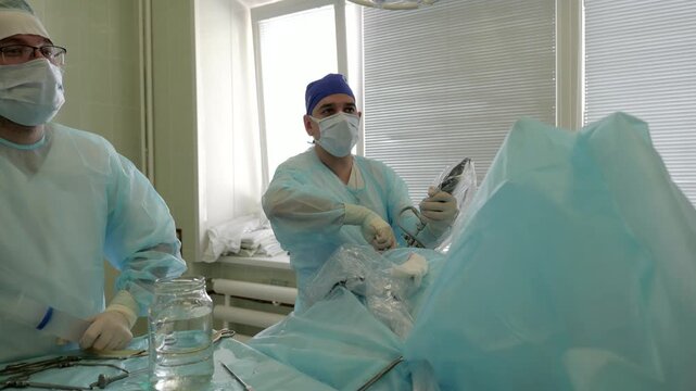 Middle sequence laparoscopic surgery with two masked surgeons performing camera insertion and instrument manipulation under soft window backlight in sterile operating room