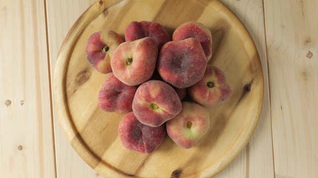 Fresh flat peaches rotating on a wooden plate