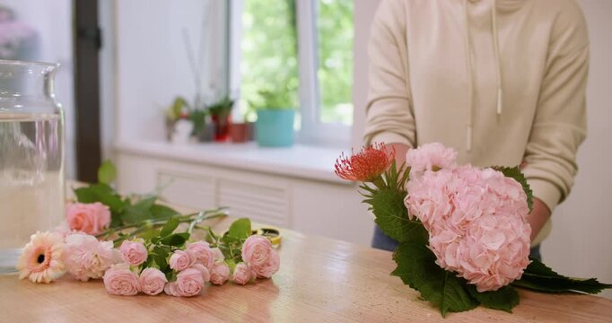 Blossom composition. Floral craft. Unrecognizable female florist arranging pink color flower hydrangea roses bouquet in professional workshop.