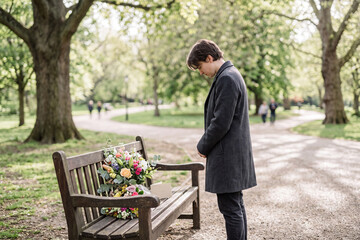 Fototapeta premium Silent grief, lone figure reflecting on mental health loss by vibrant flowers in park.