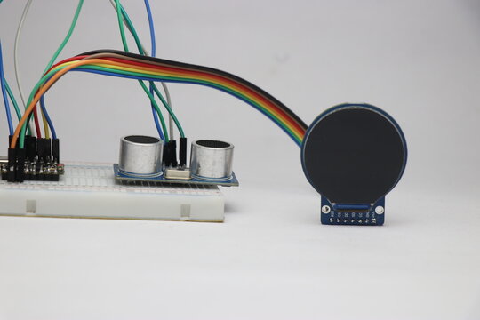 Breadboard circuit with jumper cables connected to ultrasonic distance sensor and round TFT LCD screen