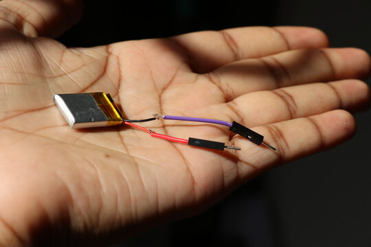 Lithium polymer battery connected with jumper wires for electronics project held in the hand
