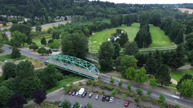 Green River passes beneath historical metal truss structures along West Meeker Street. Riverbend Golf Complex greens sprawl northward toward tree lined valley slopes in Kent, Washington