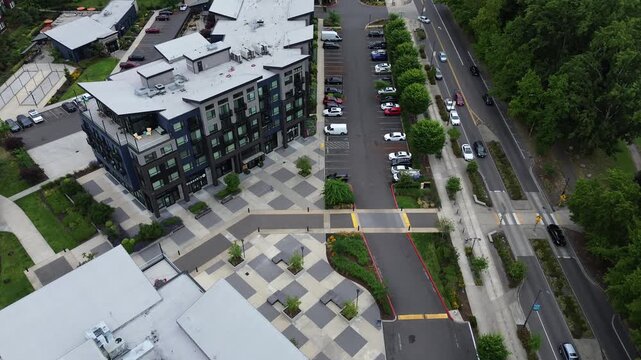 Geometric paving blocks border multi story mixed use buildings adjacent to West Meeker Street, Seattle suburbs. Parked vehicles line asphalt lanes near Riverbend Golf Complex in Kent, Washington