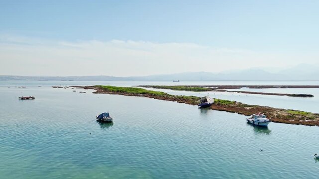 Small boats floating near wetland shoreline in shallow coastal water. Aerial view of salt marsh, lagoon shallows and calm bay