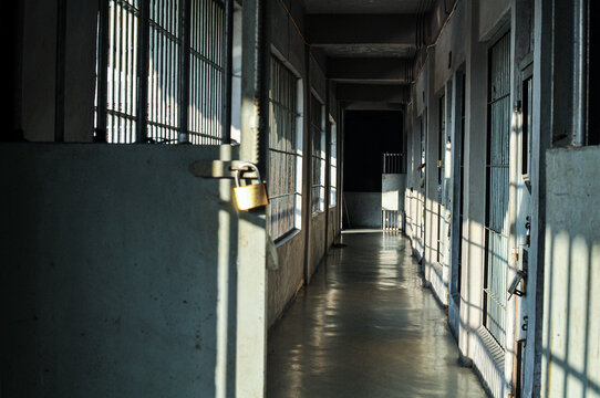 Dim prison hallway corridor with locked door brass padlock, iron bars shadow and sunlight, concept of security, correctional facility and confinement