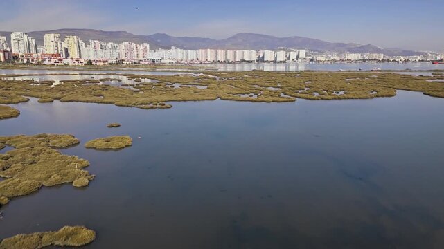 Coastal wetland and salt marsh area in Izmir Bay, Turkey. Aerial view of shallow lagoon channels near urban coastline and mountains