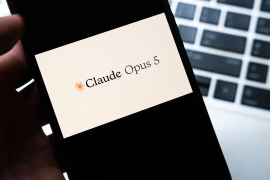 Warsaw, Poland - July 26, 2026: Claude Opus 5 AI assistant logo displayed on smartphone screen held in hand against laptop keyboard background