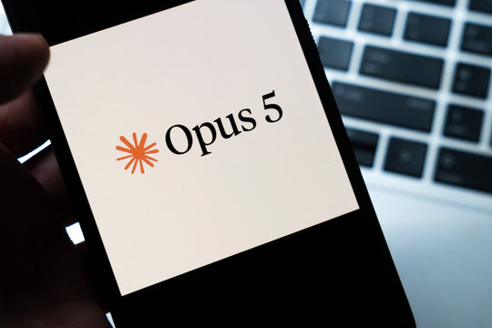 Warsaw, Poland - July 26, 2026: Opus 5 app logo displayed on smartphone screen held in hand with laptop keyboard visible in background